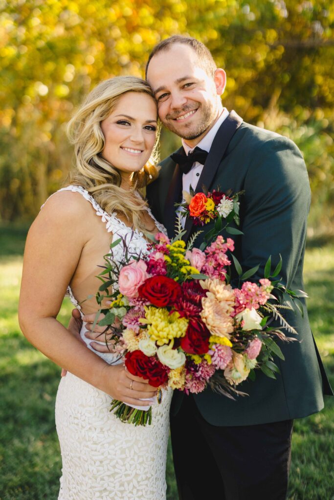 Bride and Groom smiling during their wedding portraits taken by their Kansas City Wedding Photographer. The bride is holding a beautiful colorful bouquet.