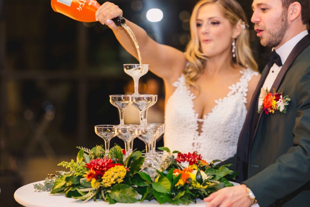 Bride pouring a custom champagne bottle into a champagne tower during her wedding reception. 