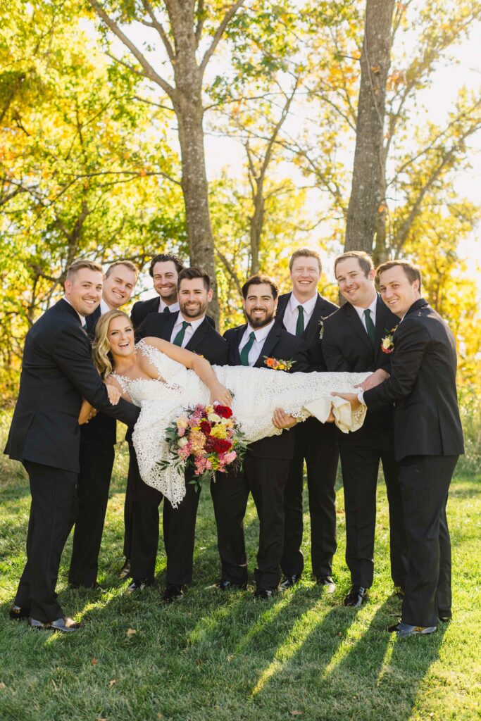 Groomsmen holding the bride in the air, smiling during their Kansas City Wedding Photographer photoshoot.