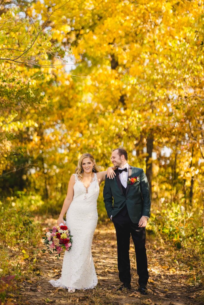 Husband and wife posing with fall foliage behind them.