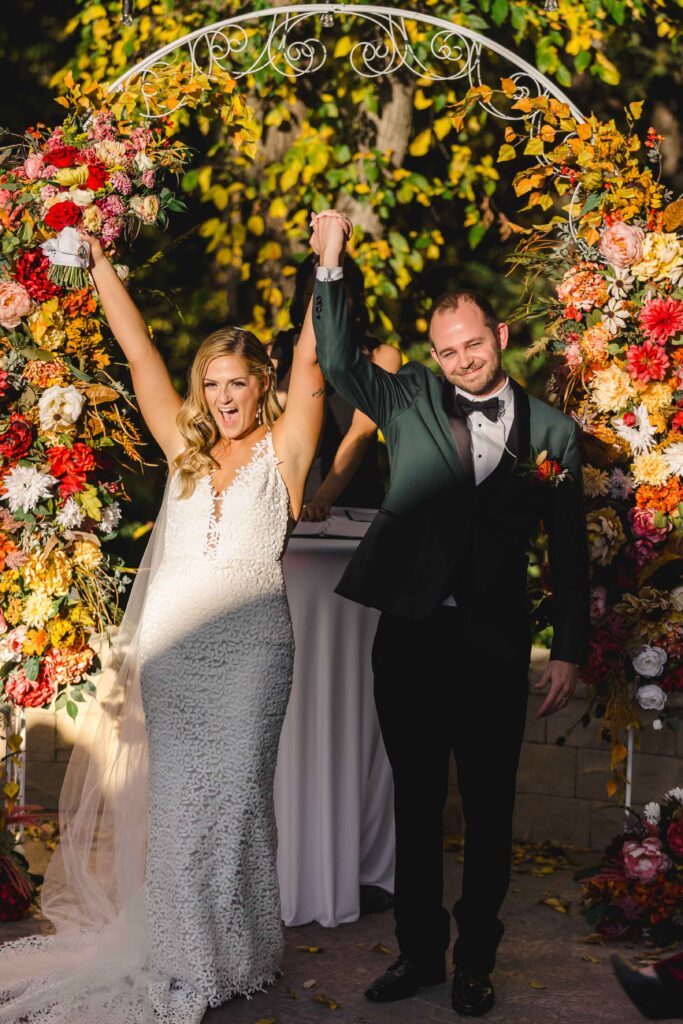 Newly weds about to walk down the aisle with their hands in the air in celebration of their marriage. 