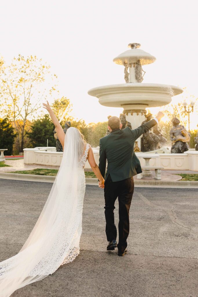 Newlyweds with their hands in the air with their backs facing the camera.