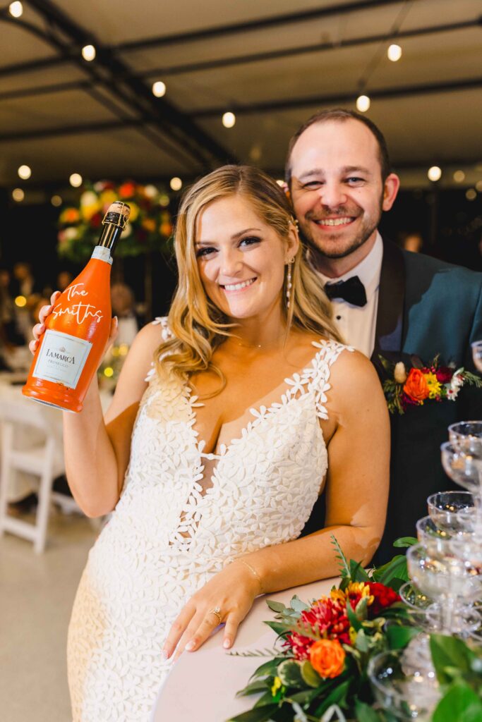 Bride and groom smiling with their custom champagne bottle.