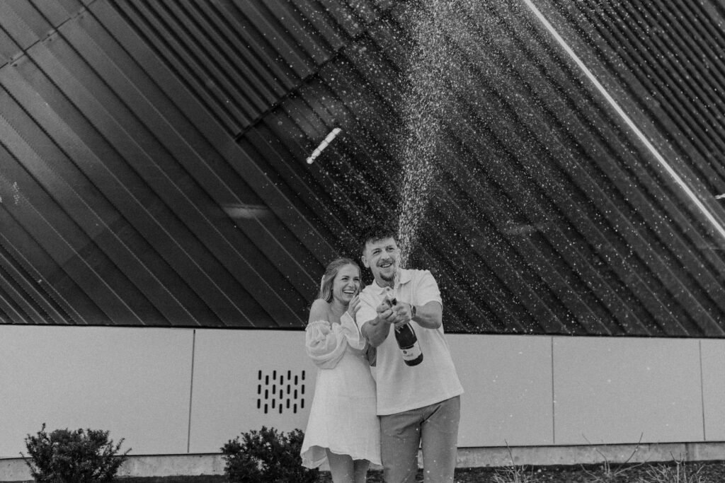 An engagement photoshoot of a couple spraying champagne to celebrate. 