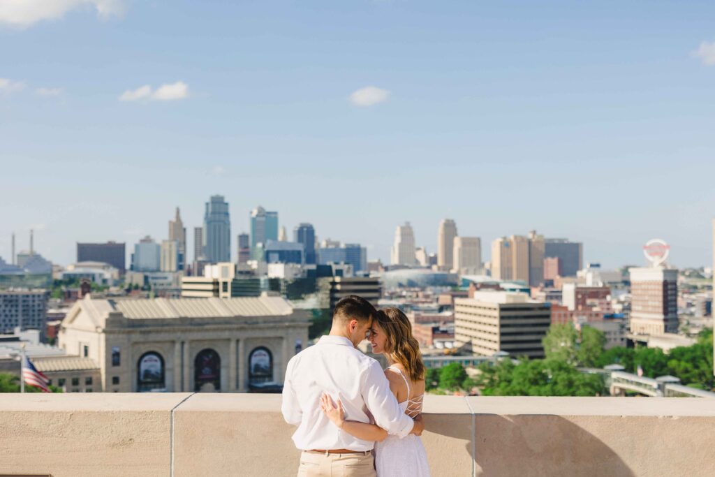 A couple looking into each others eyes with the Kansas City skyline in the background during an engagement photoshoot.