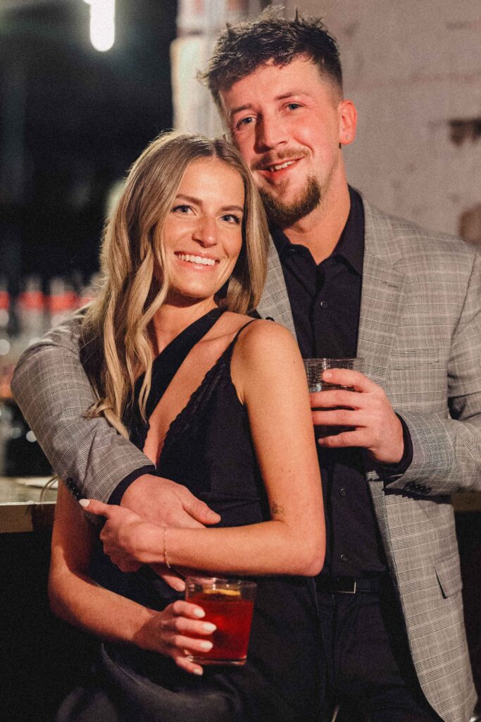 Couple holding drinks at a bar during their engagement photohoot. 