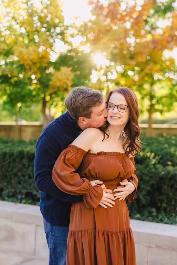 A man kissing his fiancée's neck at golden hour. 