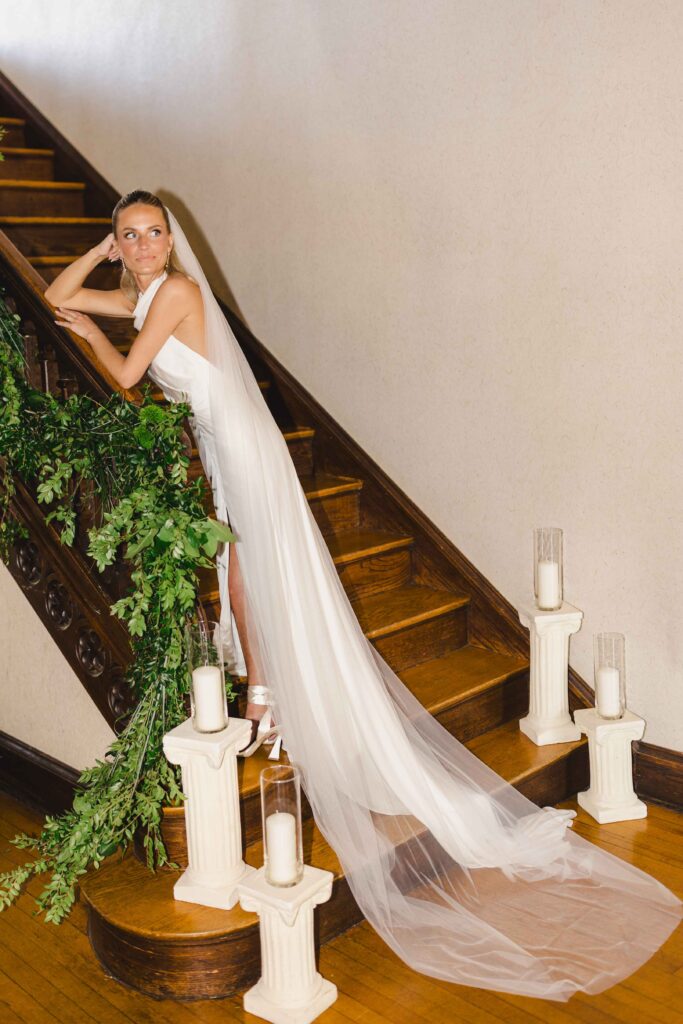 Bride posing on a staircase with her long veil trailing behind her at the Simpson House, one of the Kansas City wedding venues.