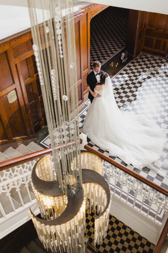 Newlyweds at the bottom of the stairs with a large chandelier at Hotel Kansas City.