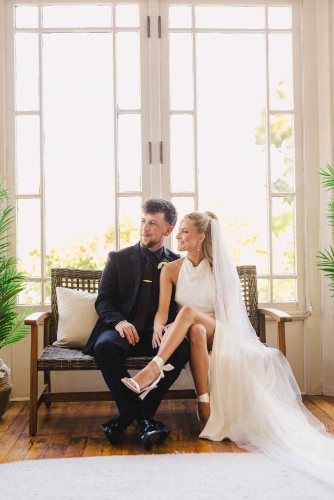 Wedding portraits in a sunroom at the Simpson House. The couple is sitting on a bench by the window.