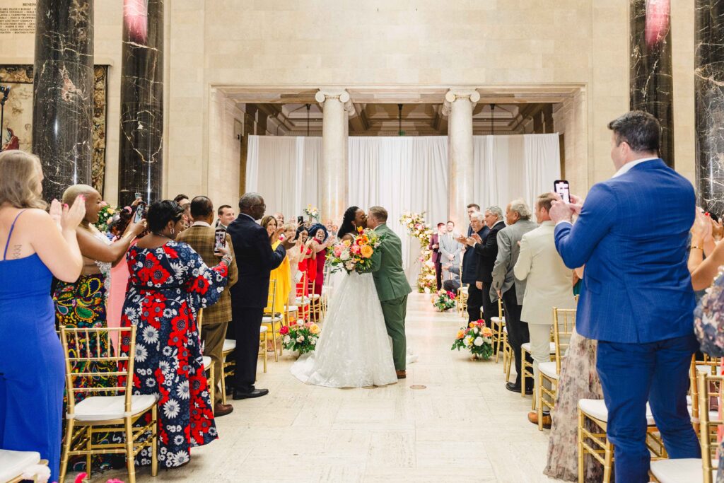 Bride and groom kissing at the end of the aisle.