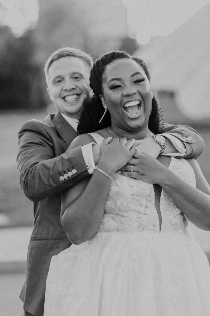 Groom wrapping his arms around the bride as she laughs during golden hour portraits. 