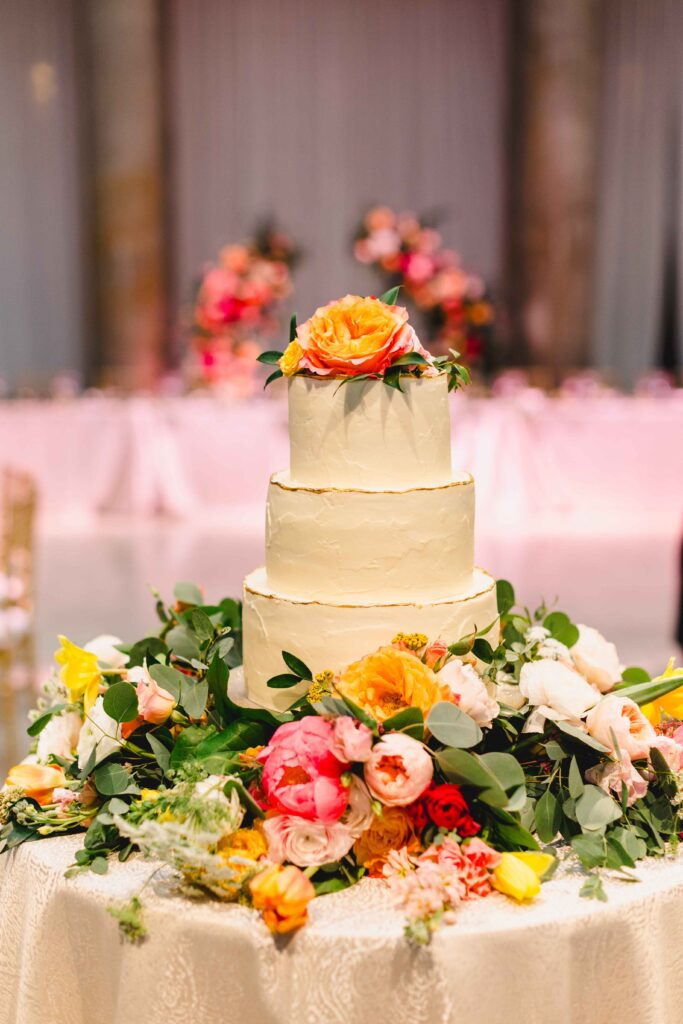 White wedding cake surrounded by pink and orange florals. 