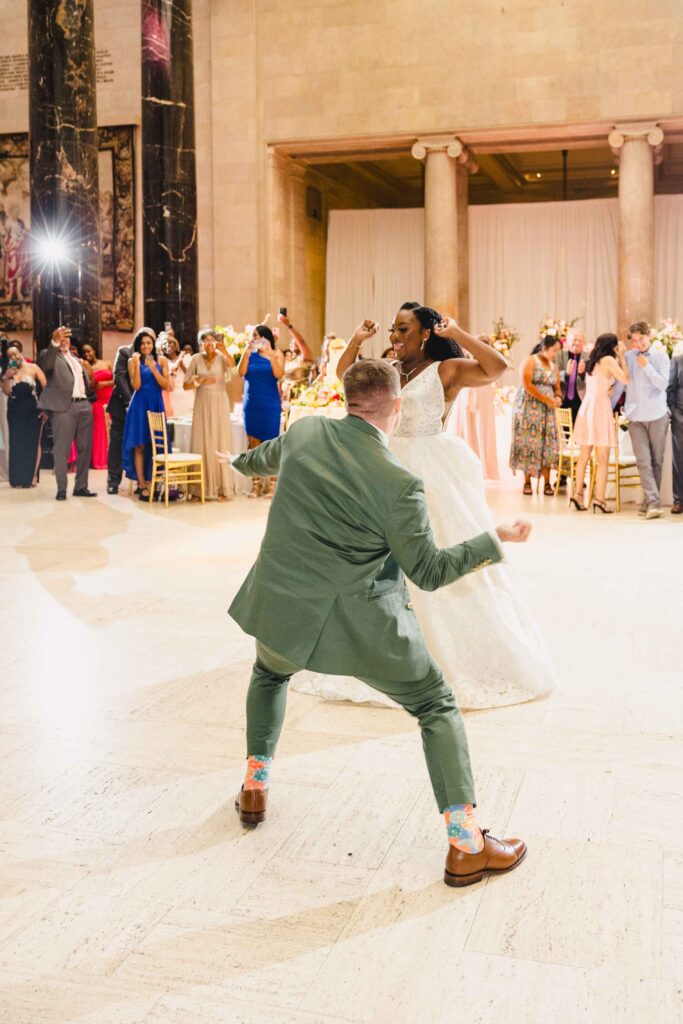 Bride and groom playfully dancing as their guests cheer. 