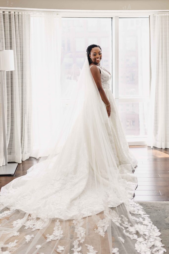 Bride smiling after putting on her wedding gown and cathedral-length veil. 