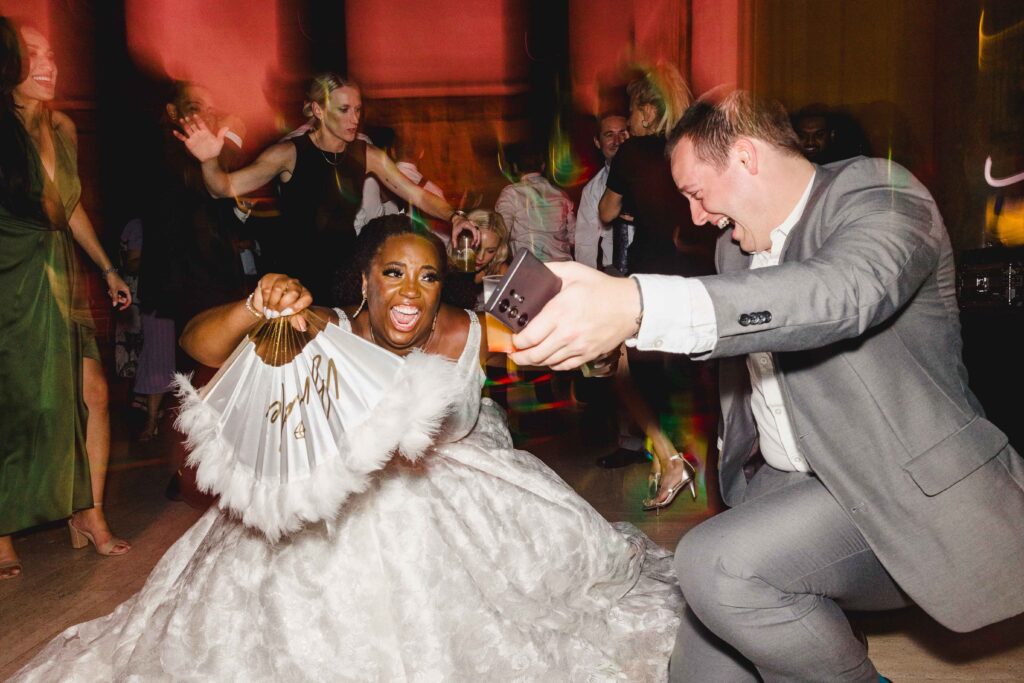 Bride and a wedding guest dropping low and laughing as they dance at their Nelson Atkins wedding.