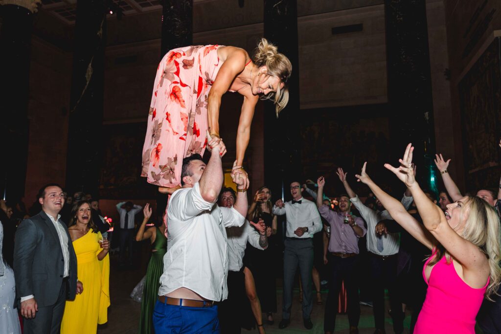 A wedding guest standing on a mans shoulders on the dance floor. 