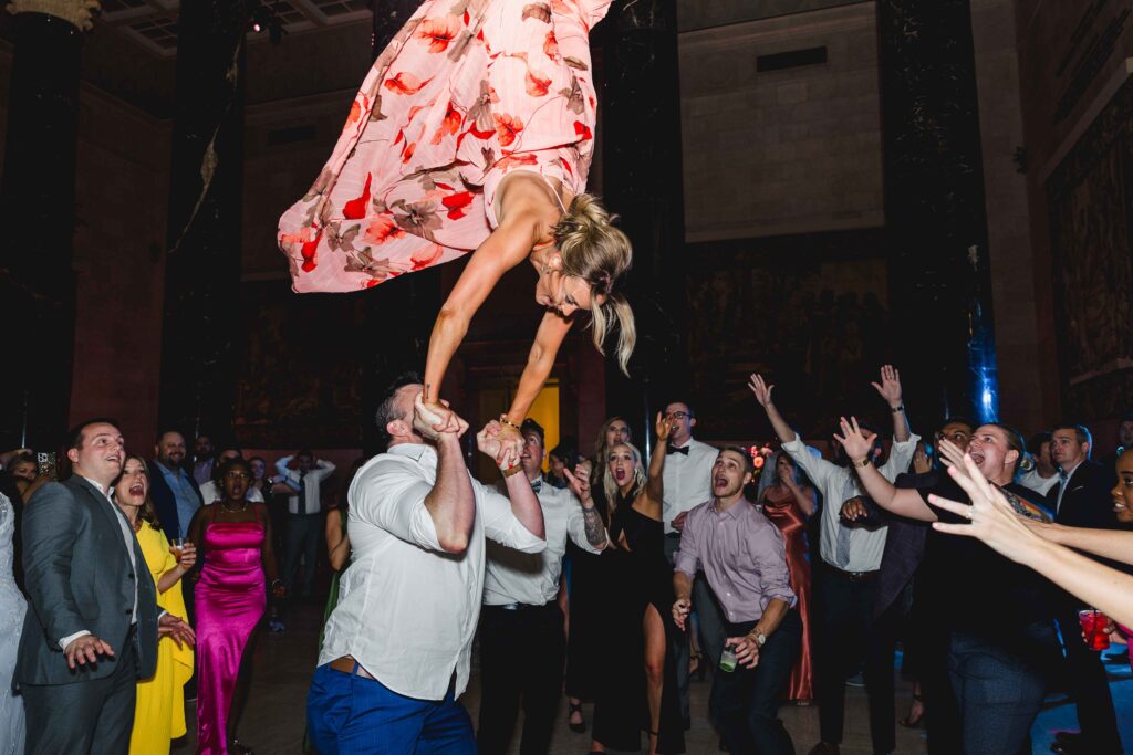 A wedding guest doing a flip off a mans shoulders on the dance floor of the Nelson Atkins wedding.