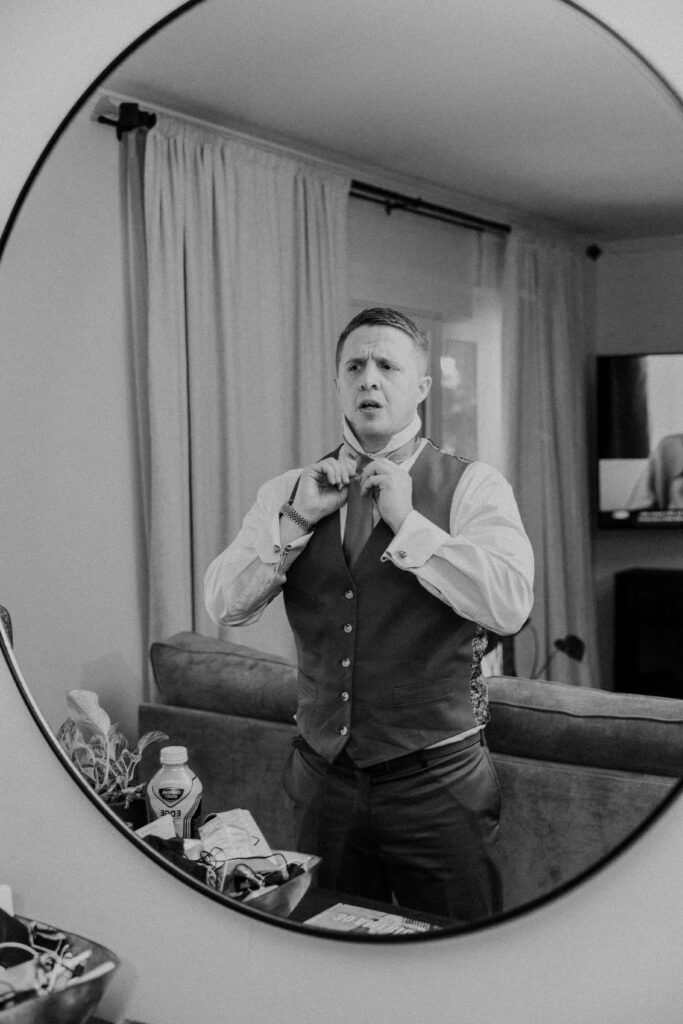 Groom putting on his tie in the mirror.