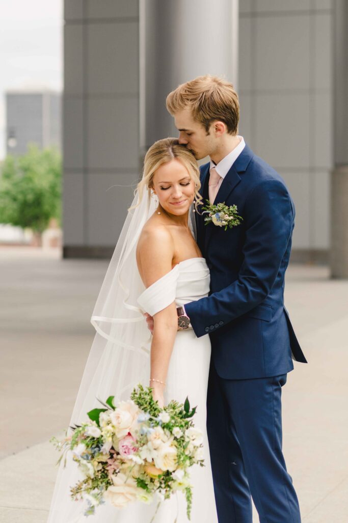 Groom kissing the top of the brides head before referring to their wedding family photos list.