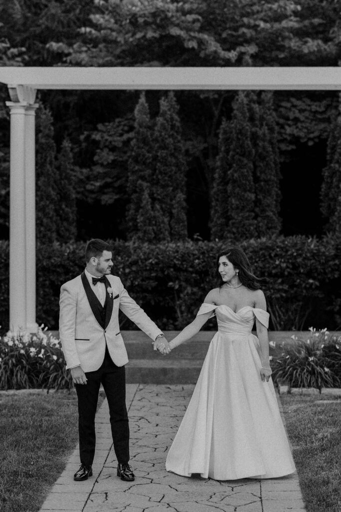 Bride and groom standing hand in hand in a garden.