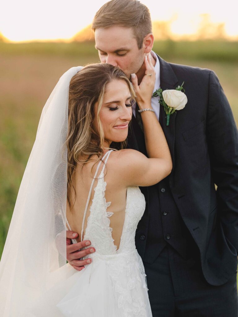 Groom kissing the brides head at sunset.