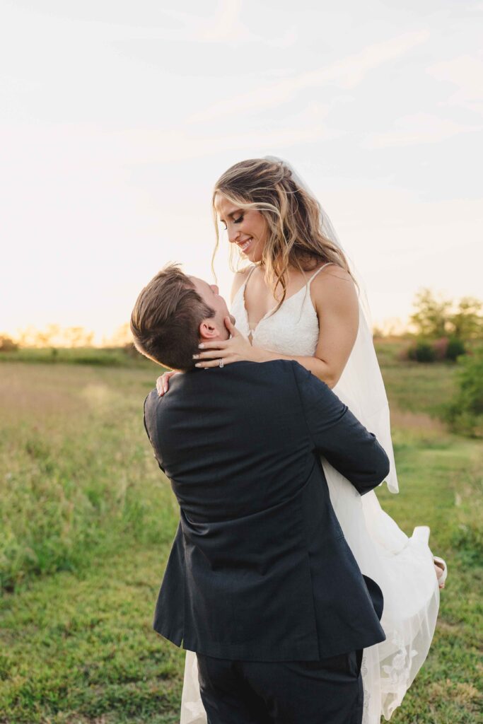 Groom holding the bride in a field at sunset.