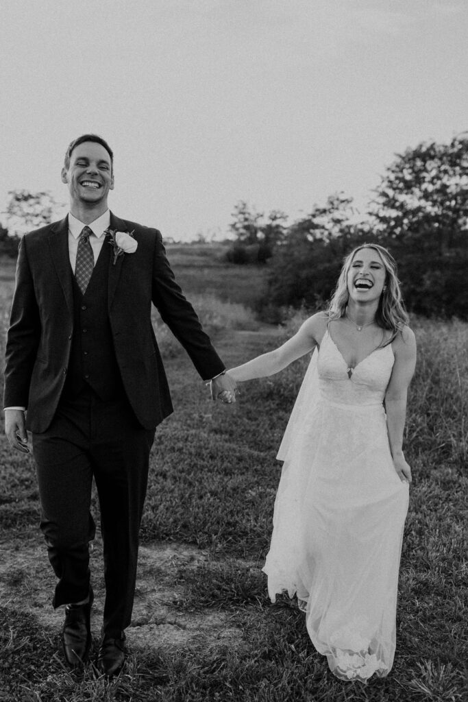 Bride and groom laughing and holding hands in a field. 