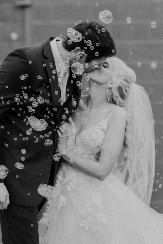 The newlyweds kissing with bubbles floating in the air.