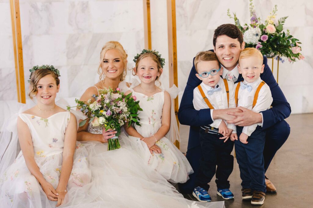 Bride and groom smiling with young kids which was planning during their wedding family photos list.