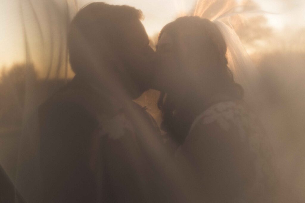 Newlyweds kissing romantically under the bride's veil. 