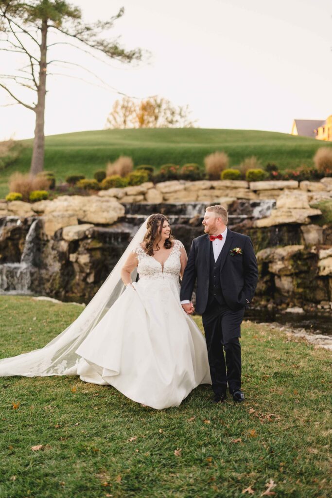 Bride and groom smiling and walking in front of a waterfall at the Oakwood Country Club.