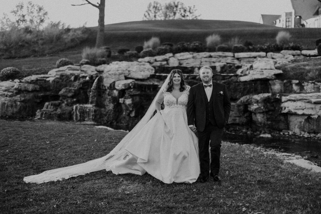 Newlyweds smiling in front of a small waterfall at the Oakwood Country Club.