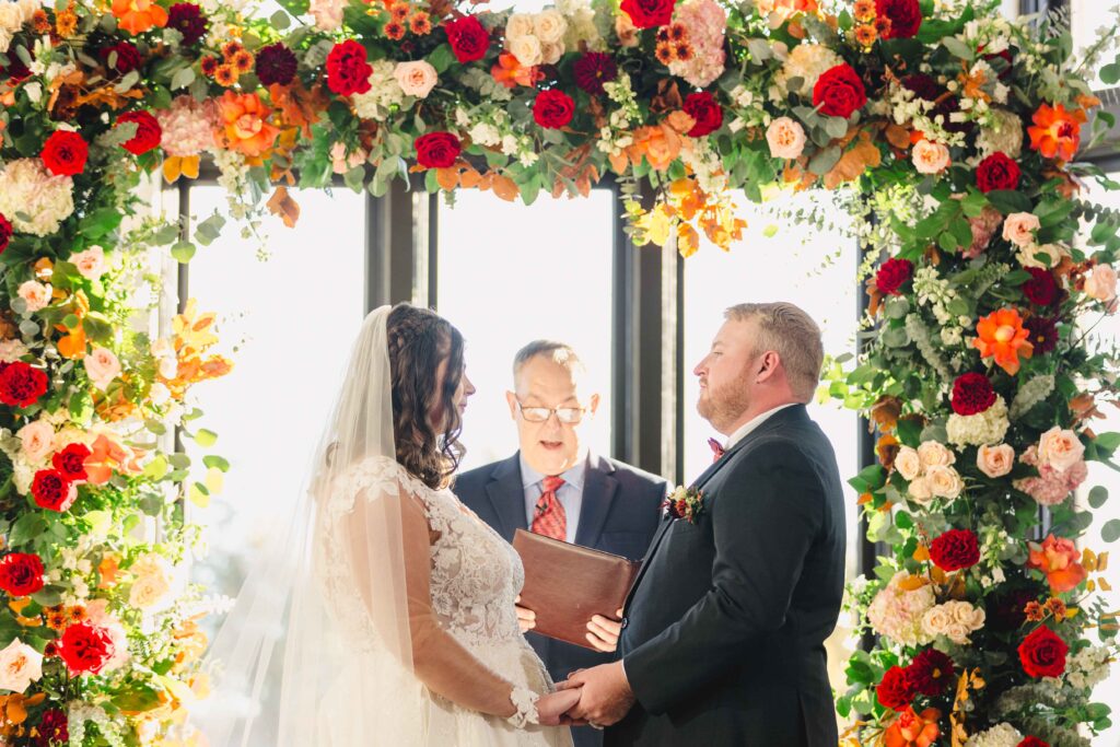 Bride and groom at the altar of their Oakwood Country Club wedding surrounded by vibrant florals. 