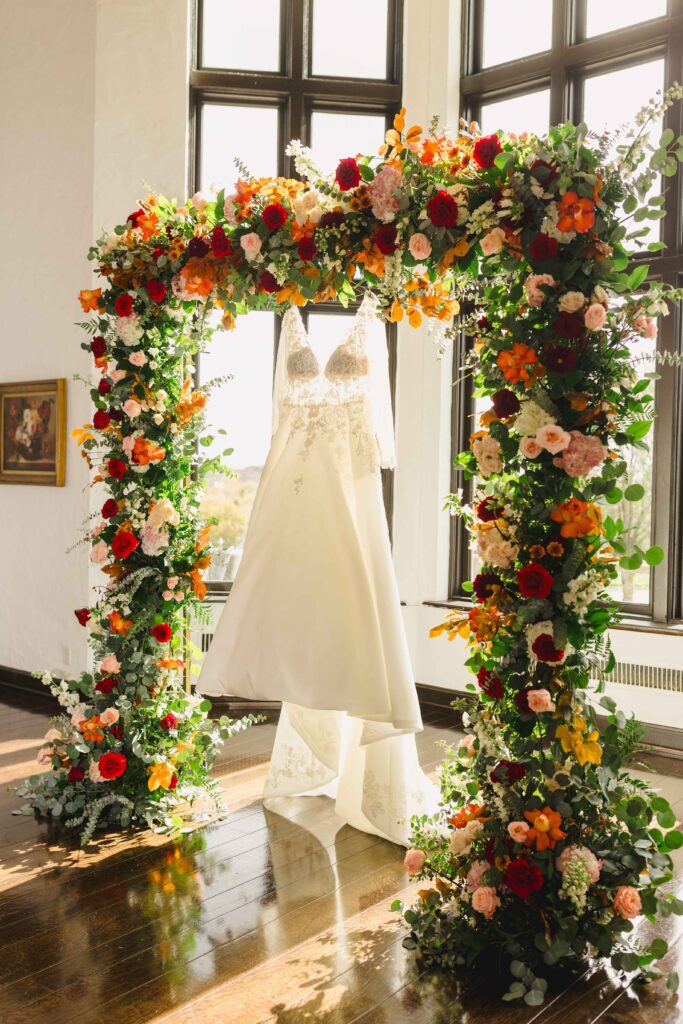 The bride's wedding dress hanging on the floral wedding arch at the altar. 