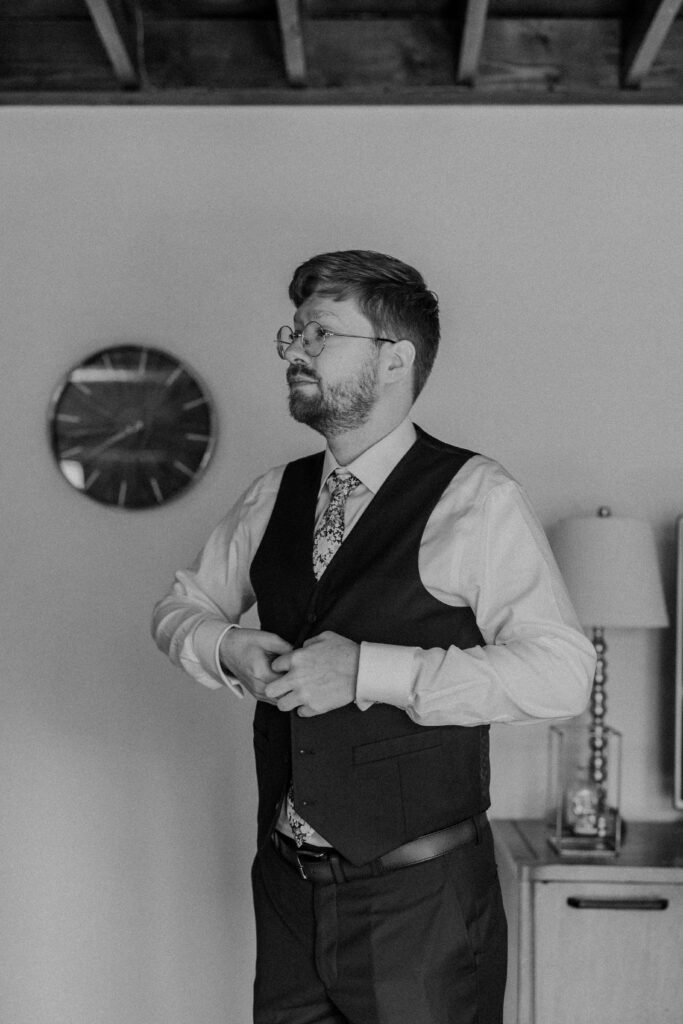 Groom buttoning his wedding vest. 