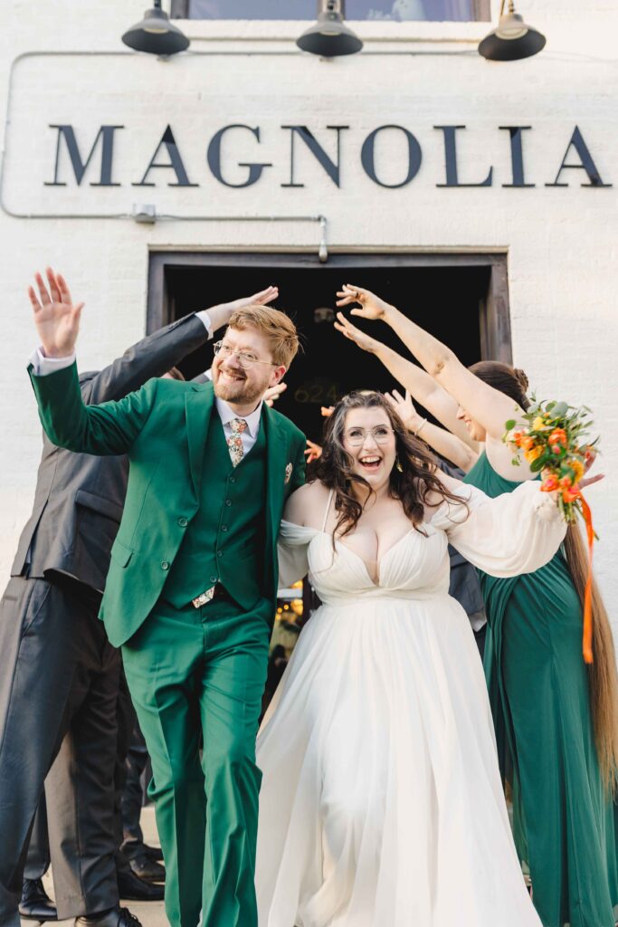 Bride and groom exiting their wedding ceremony while the wedding party cheers. 