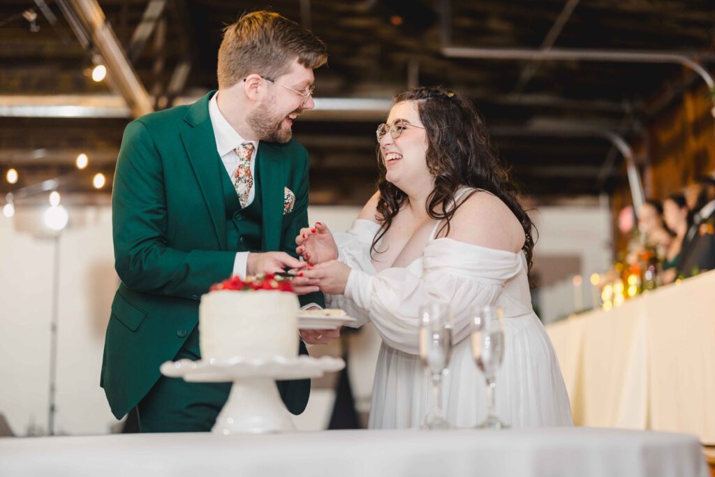 Bride and groom cutting cake and laughing together at their Kansas City wedding.