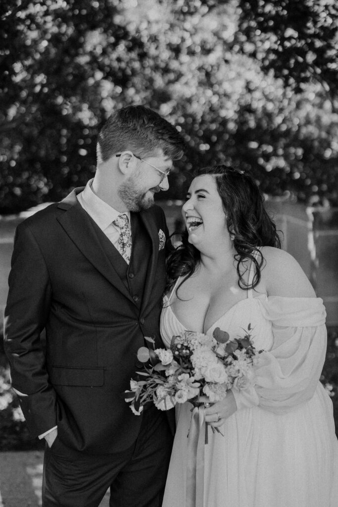 Bride and groom laughing and smiling surrounded by greenery. 