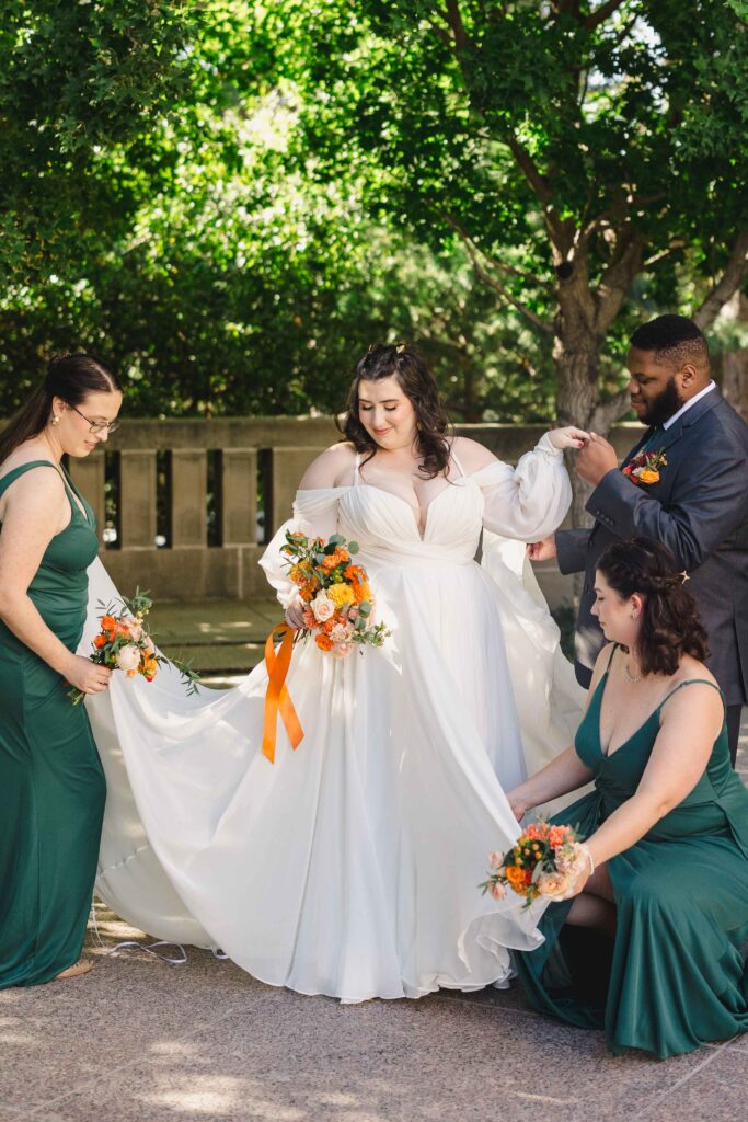 Bridal party helping the bride with her dress while holding beautiful flowers. 