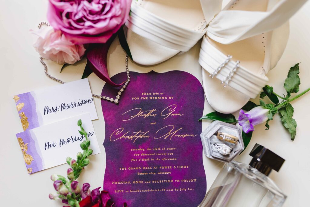 Detail shot of the wedding invitation, heels, rings, and perfume.