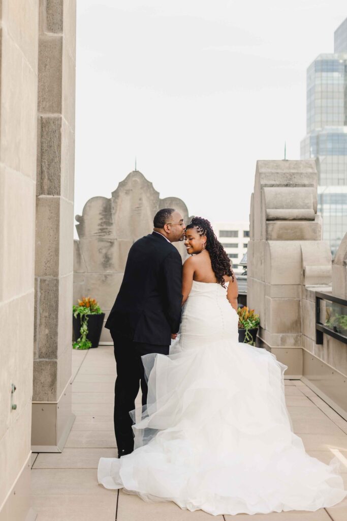 Groom kissing his bride on the rooftop with downtown Kansas City in the background.