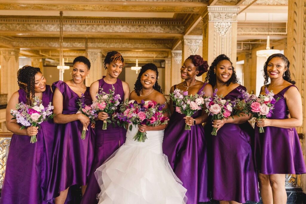 Bride and her bridesmaids smiling while wearing deep purple dresses.