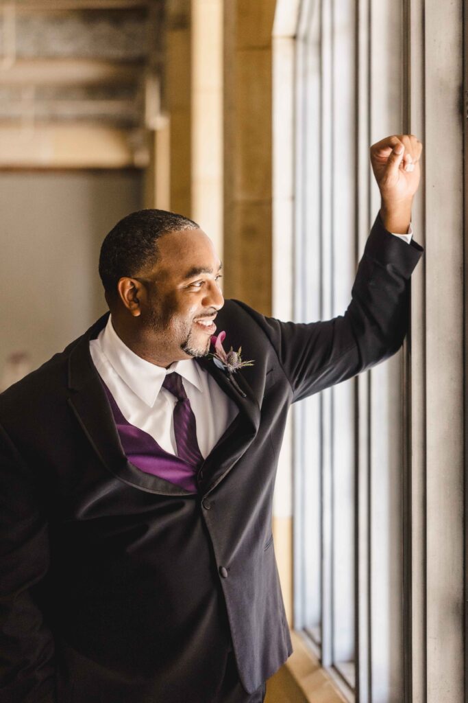 Groom looking out the window in his wedding attire.