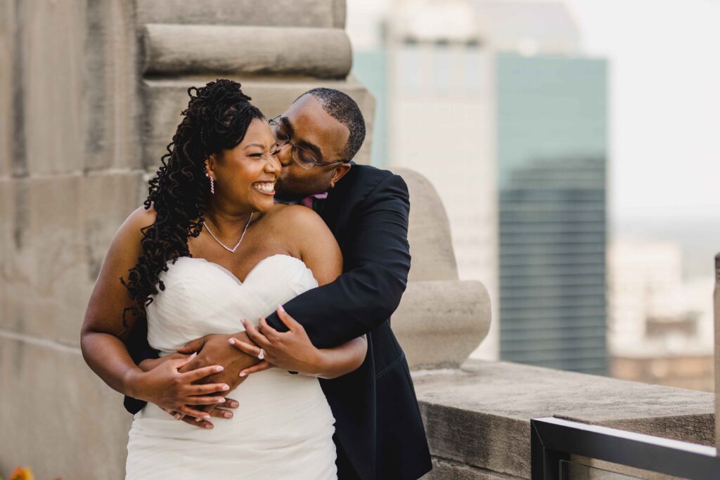 Groom kissing his bride's cheek and hugging her on the rooftop of The Grand Hall at Power & Light.