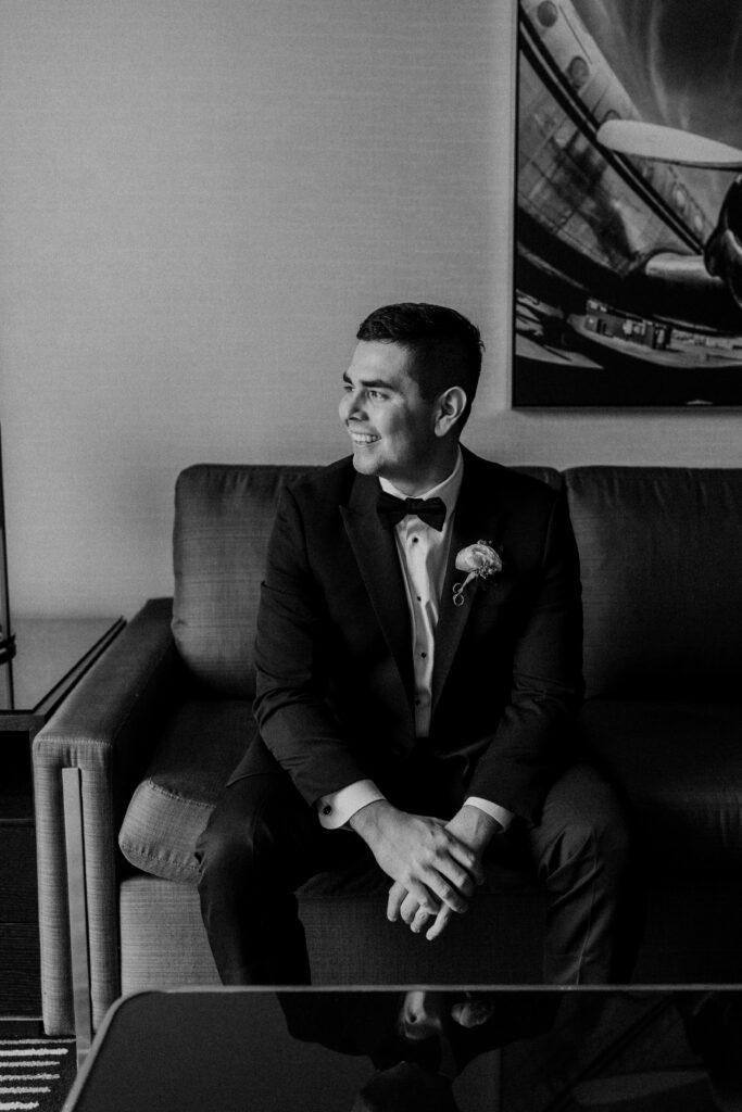 Groom sitting in his wedding suit and smiling.