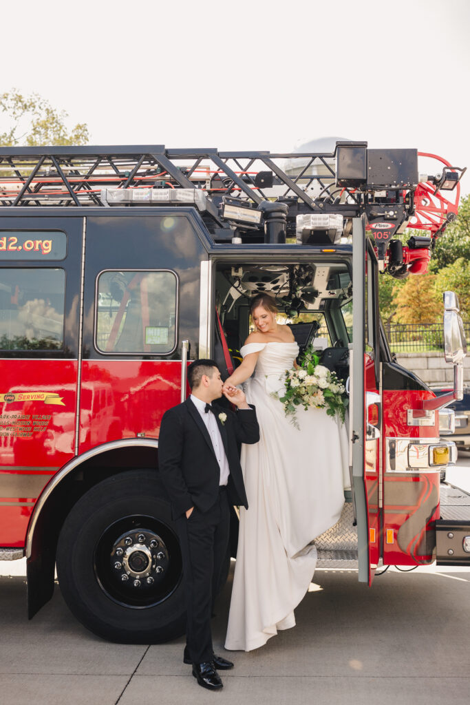 Groom kissing his wife's hand as she sits in a fire truck.