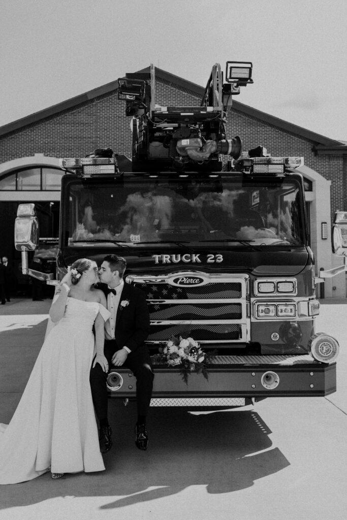 Bride and groom kissing while leaning on a fire truck for unique wedding photos before their reception at The Guild KC.