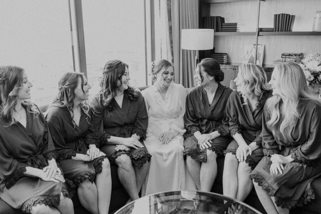 Bride and bridesmaids smiling at one another in robes.