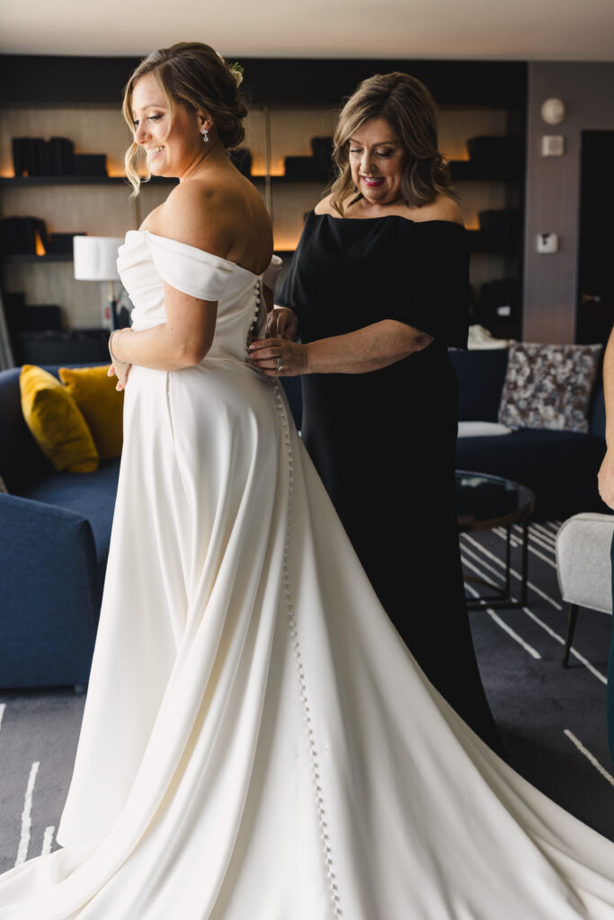 Mother of the bride helping the bride button her wedding dress before the wedding at The Guild KC.